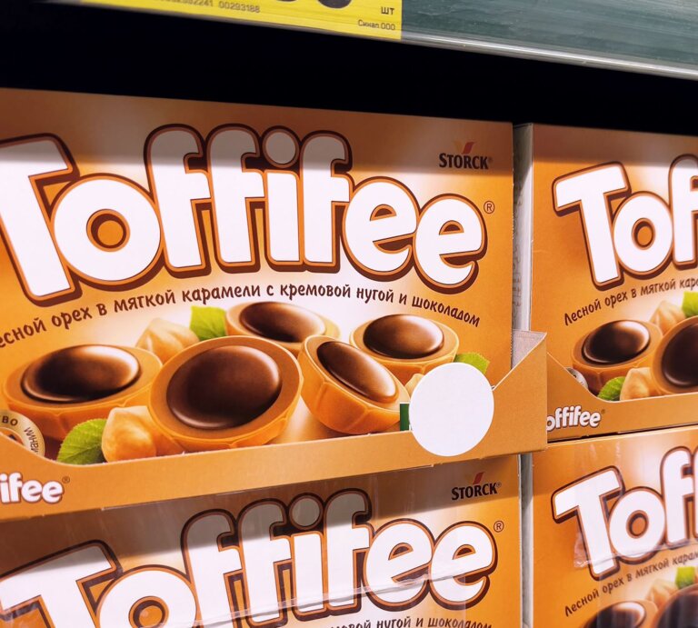 Nahaufnahme eines Supermarktregals mit orangefarbenen Toffifee-Schachteln und Preisschildern in kyrillischer Schrift. | © Adobe Stock/ Fanta Media