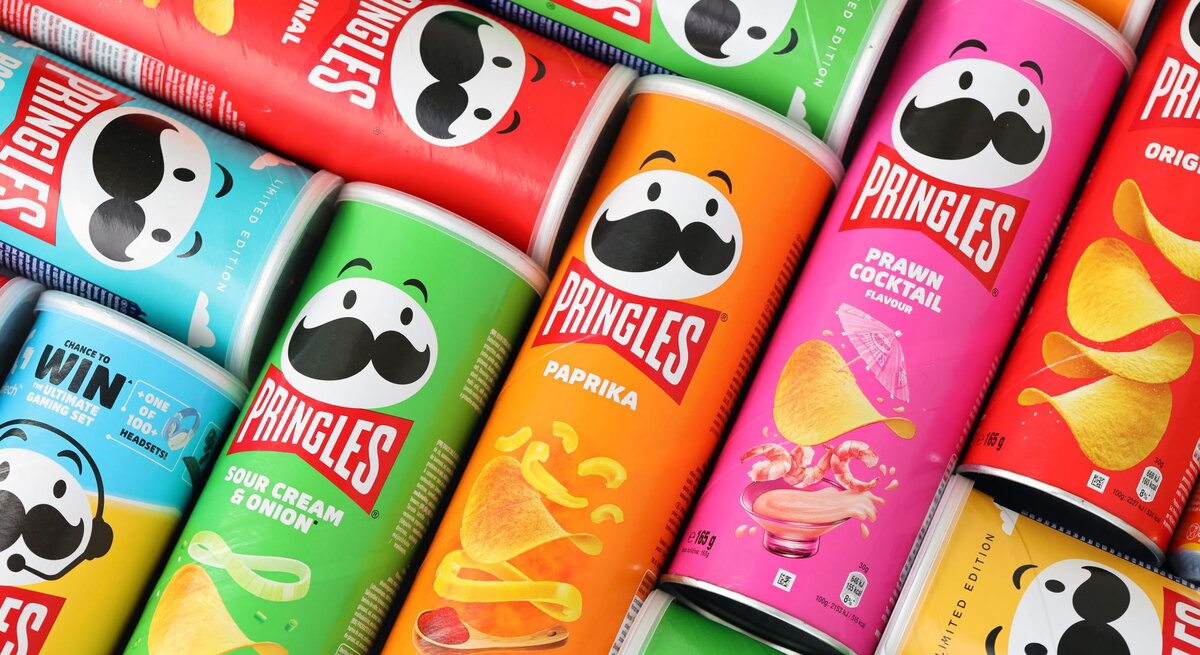 Bunte Pringles-Dosen in verschiedenen Geschmacksrichtungen wie Paprika, Sour Cream und Prawn Cocktail liegen nebeneinander aufgereiht.