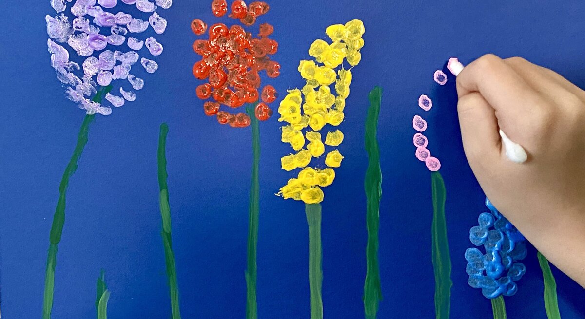 Kinderhand malt bunte Blumen mit Wattestäbchen auf dunkelblauem Hintergrund