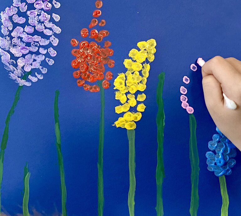 Kinderhand malt bunte Blumen mit Wattestäbchen auf dunkelblauem Hintergrund | © Getty Images/4u4me