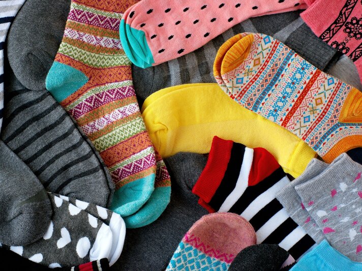 Bunte Socken mit verschiedenen Mustern und Farben liegen chaotisch auf einem grauen Untergrund. | © Getty Images/Eugene4873