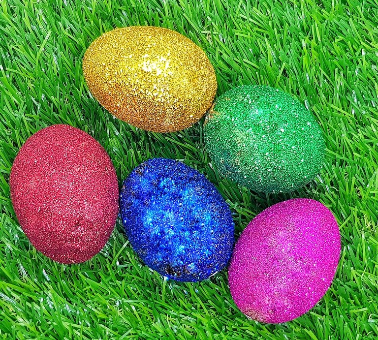 Fünf glitzernde Ostereier in Rot, Blau, Grün, Gold und Pink liegen dicht beieinander auf frischem, leuchtend grünem Gras. | © Shutterstock/icyyoke