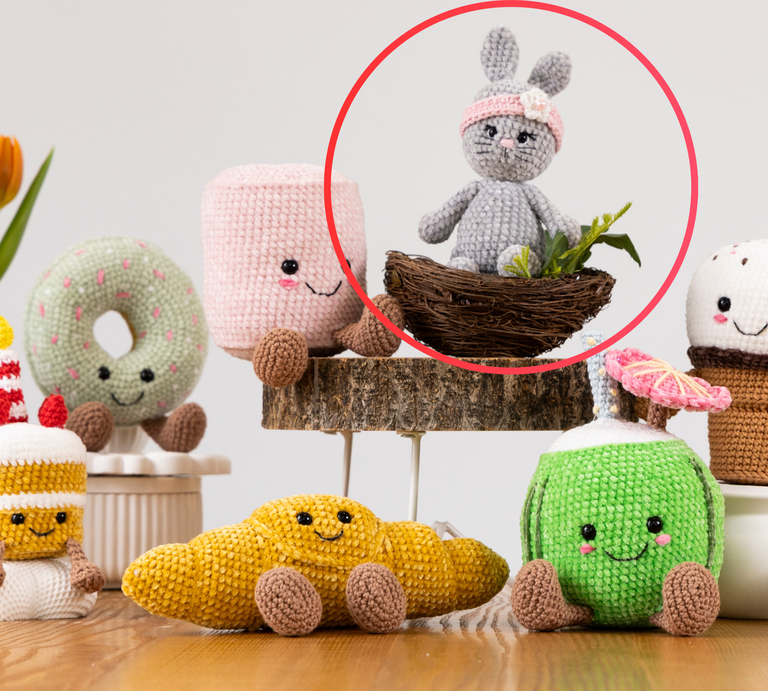 Ein gehäkelter grauer Hase mit rosa Stirnband und Blüte sitzt in einem kleinen Vogelnest, umgeben von grünen Pflanzen auf einem Holzpodest. | © BILD der FRAU/Photoproduction Bernd Hanselmann