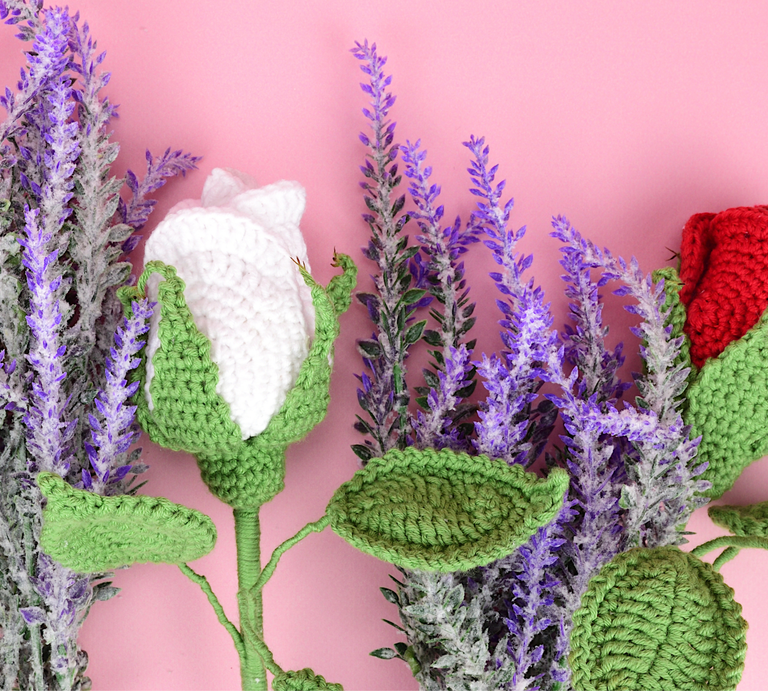 Handgehäkelte Blume mit grünen Blättern, weißen und roten Blüten vor einem Arrangement aus lilafarbenem Lavendel auf rosa Hintergrund. | © Canva