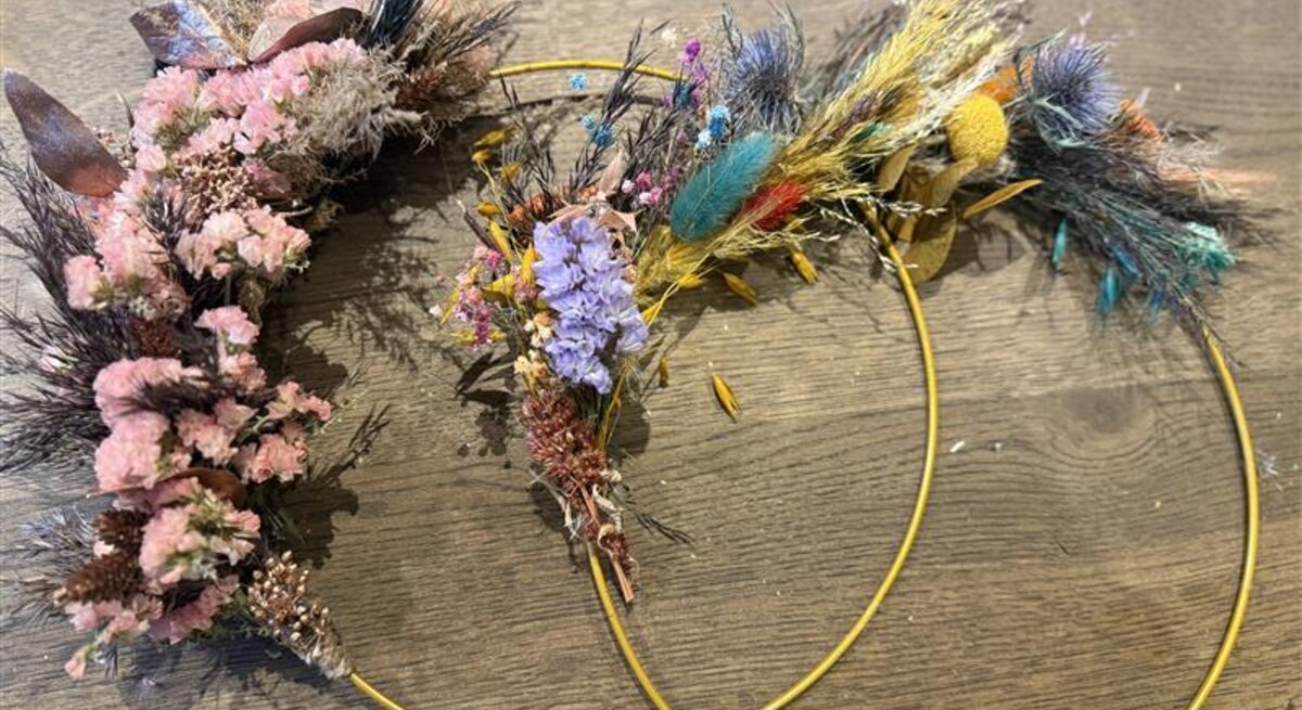 Dekokränze mit Trockenblumen auf einem Holztisch, bestehend aus bunten Blumen wie lila, rosa, gelben und grünen Naturmaterialien.