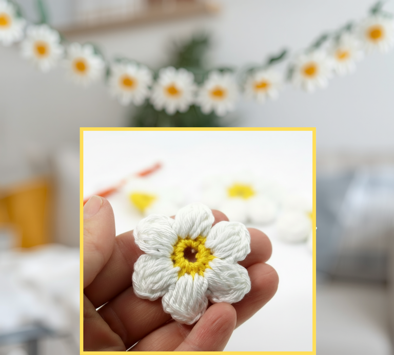 Hand hält kleine gehäkelte Blume mit weißen Blütenblättern und gelber Mitte, im Hintergrund unscharf weitere Blumen und Wohnraum. | © Canva / AI [M]