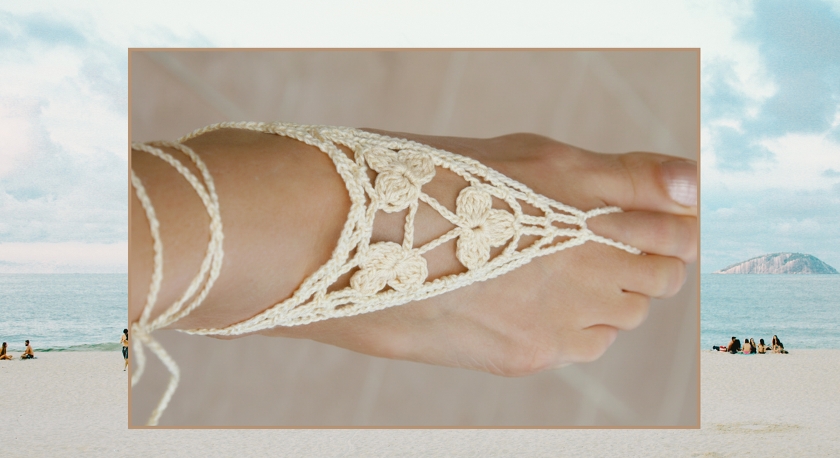 Nahaufnahme eines Fußes mit filigranen Sandalenschmuck aus beigem Häkelmuster vor hellem Hintergrund, eingebettet in eine Strandszene.