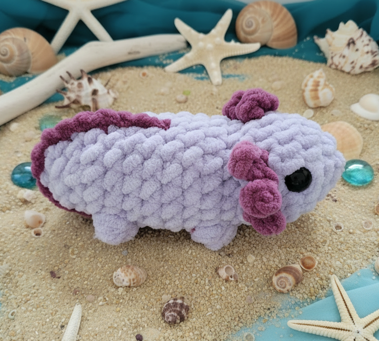 Ein lilafarbenes gehäkeltes Axolotl mit violetten Fransen liegt auf dekorativem Sand, umgeben von Muscheln und Sternen. | © Getty Images (Katelyn Pouliot / 500px) / AI [M]