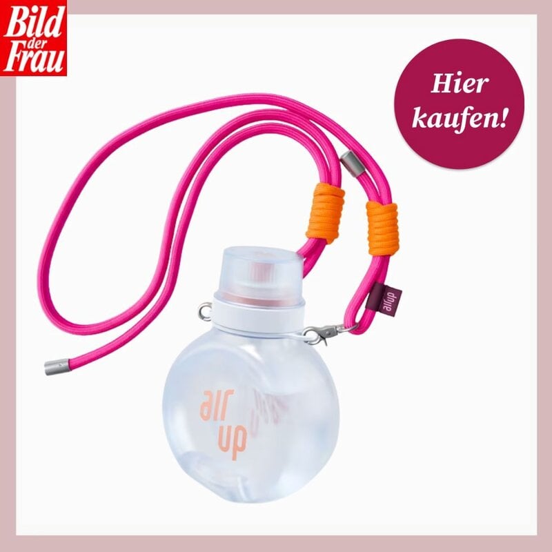 Transparente Trinkflasche mit weißem Verschluss und pinker Kordel mit orangefarbenen Wicklungen vor hellem Hintergrund. | © air up/Canva/Collage:bilderfrau.de