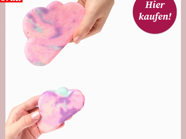 Zwei weibliche Hände halten pastellfarbene Badebomben in Wolkenform vor weißem Hintergrund, eine rosa, eine lila-blau gemustert. | © Lush/Canva/Collage:bildderfrau.de