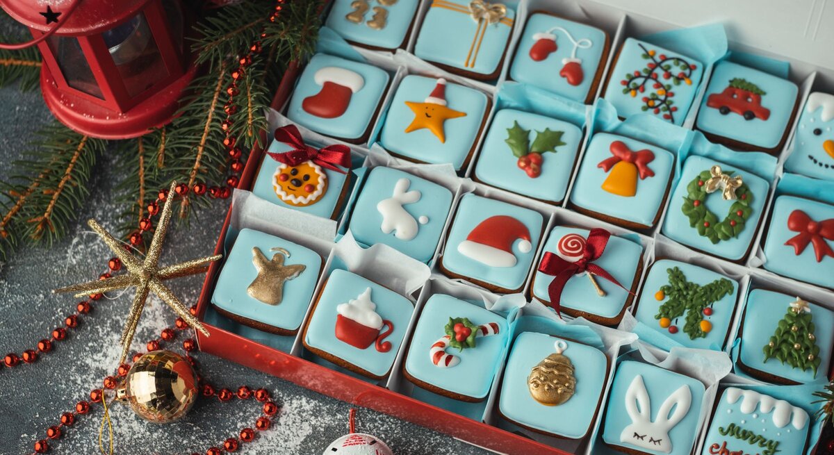 Detailreicher Adventskalender mit 24 bunt verzierten Weihnachtskeksen in Blau, Rot und Gold in festlicher Geschenkbox.