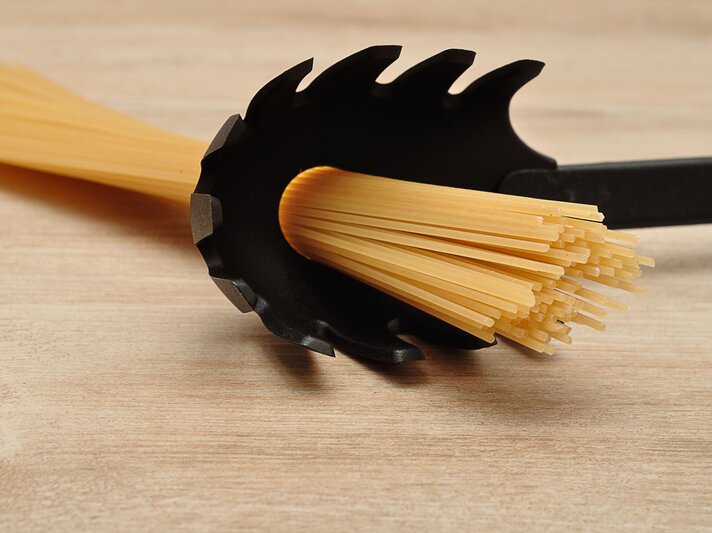 Ungekochte Spaghetti werden in einem schwarzen Pastalöffel auf heller Holzoberfläche exakt portioniert gehalten. | © Shutterstock/Marietjie