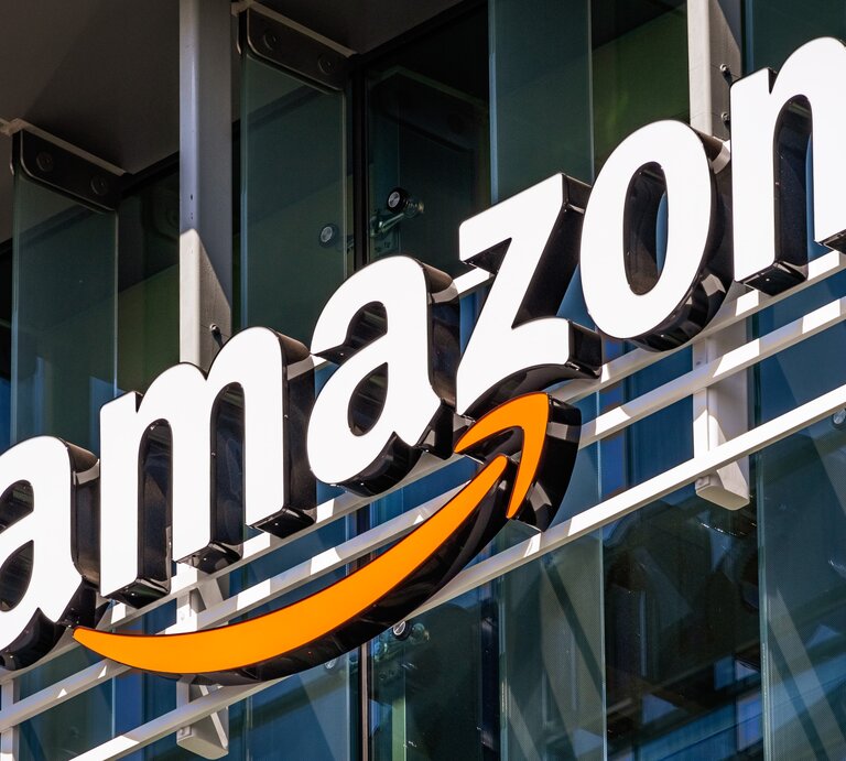 Nahaufnahme des bekannten Amazon-Schriftzugs mit orangem Pfeil auf Gebäudefront. | © AdobeStock/ Sundry Photography