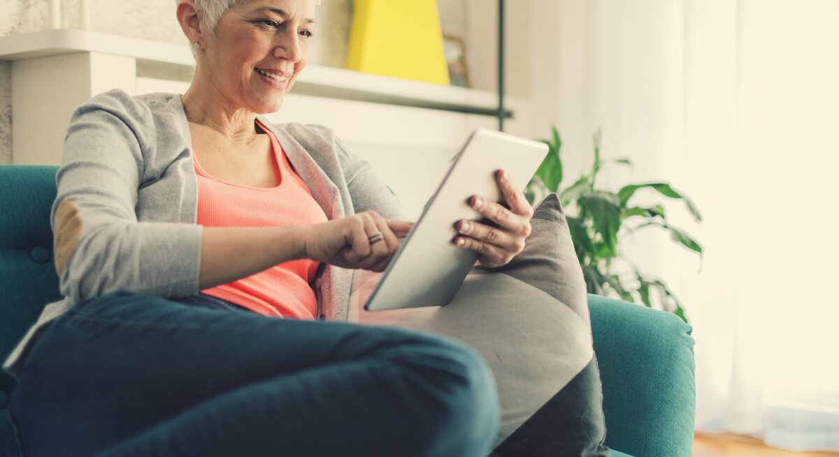 Frau guckt ein Tablet und sitzt auf dem Sofa.