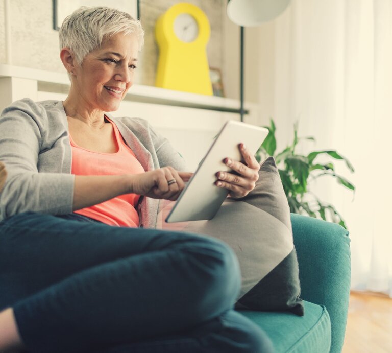 Frau guckt ein Tablet und sitzt auf dem Sofa. | © gettyimages/ vgajic