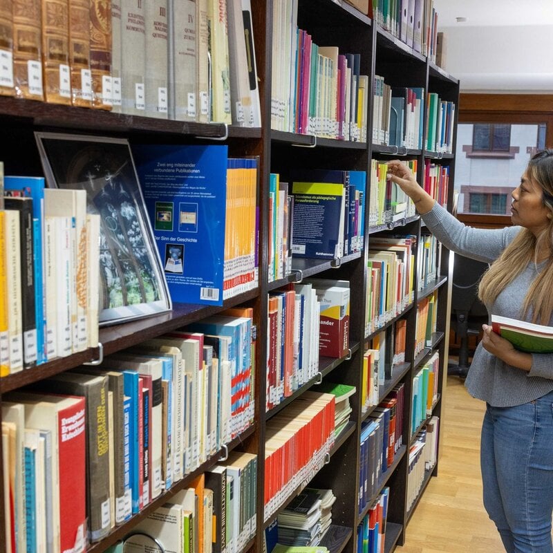 Eine Frau steht vor einem Bücherregal und hält Bücher in der Hand | © BILD der FRAU
