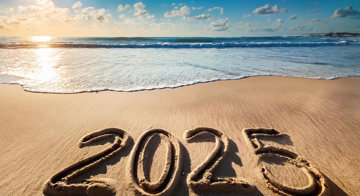 Die Zahl „2025“ ist in nassen Sand am Strand geschrieben, während Sonnenstrahlen das ruhige Meer im Hintergrund erhellen.