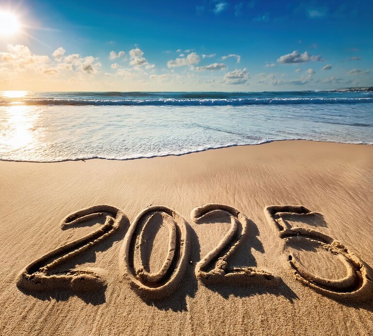 Die Zahl „2025“ ist in nassen Sand am Strand geschrieben, während Sonnenstrahlen das ruhige Meer im Hintergrund erhellen. | © Adobe Stock/Arda ALTAY (KI-generiert)