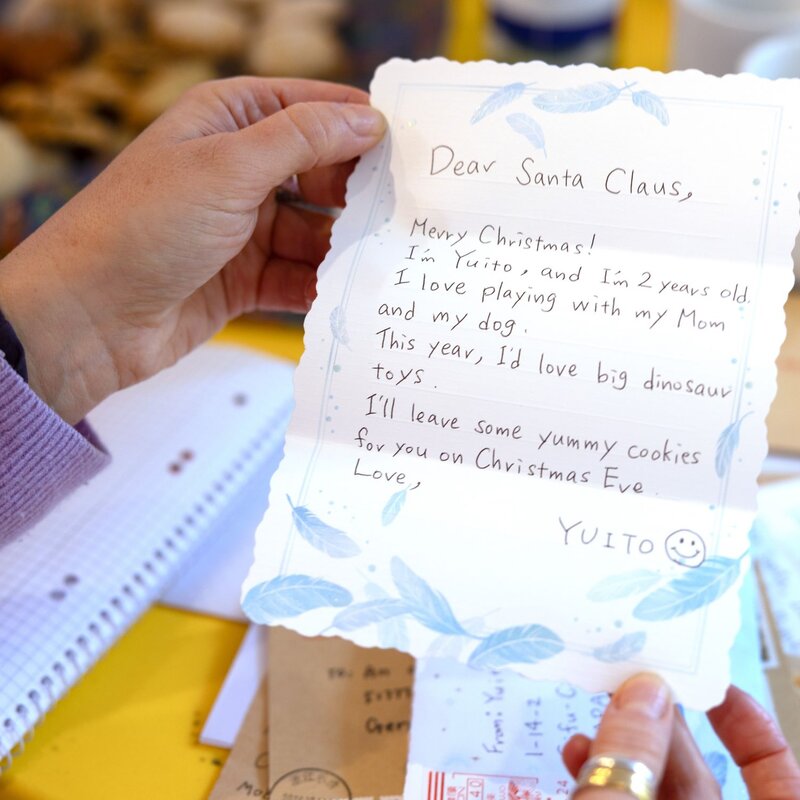 Eine Hand in einem fliederfarbenen Pullover hält einen handgeschriebenen Weihnachtsbrief an den Weihnachtsmann, im Hintergrund Kekse und Briefe. | © BILD der FRAU 