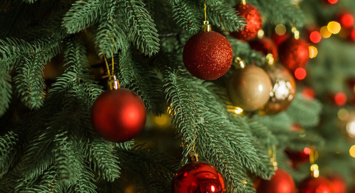 Nahaufnahme eines geschmückten künstlichen Weihnachtsbaumes mit roten und goldenen Weihnachtskugeln vor unscharfem, warm beleuchtetem Hintergrund.