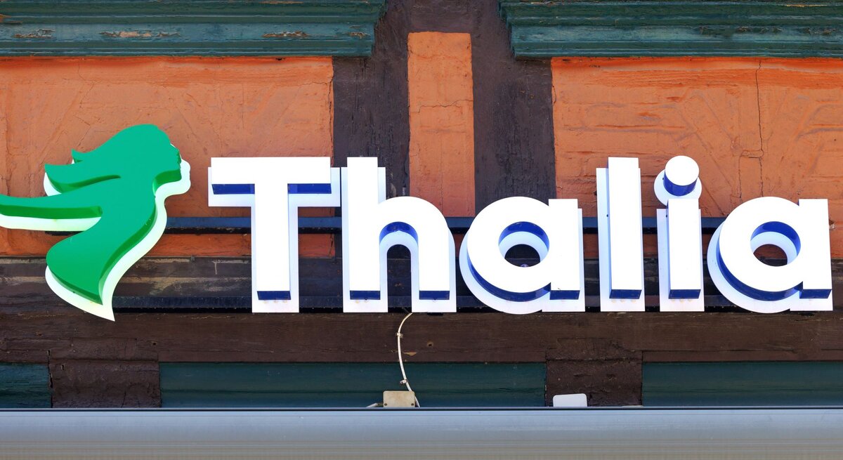 Leuchtreklame der Buchhandlung Thalia mit grünem Logo auf Fachwerkfassade eines Gebäudes in warmen Farben.