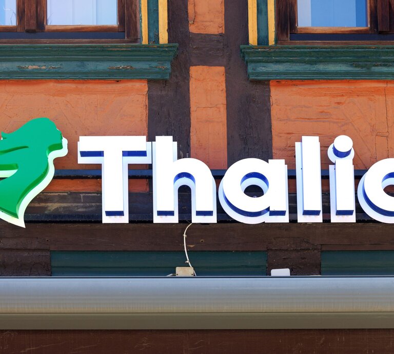Leuchtreklame der Buchhandlung Thalia mit grünem Logo auf Fachwerkfassade eines Gebäudes in warmen Farben. | © Shutterstock/Birgit Reitz-Hofmann