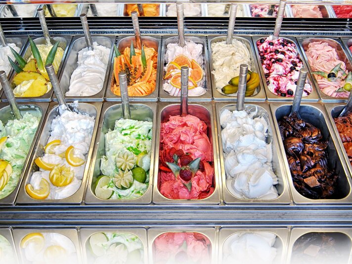 Verschiedene Sorten Eiscreme in Metallbehältern, dekoriert mit Obstscheiben, darunter Zitrone, Limette und Erdbeeren. | © iStock.com/Photology1971