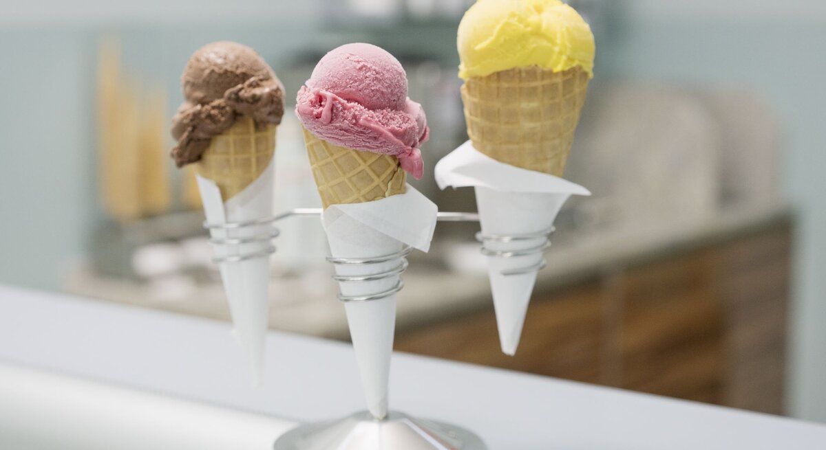 Drei Eiswaffeln mit Schokoladen-, Himbeer- und Zitroneneis stehen nebeneinander in einem modernen Halter auf einer Theke.