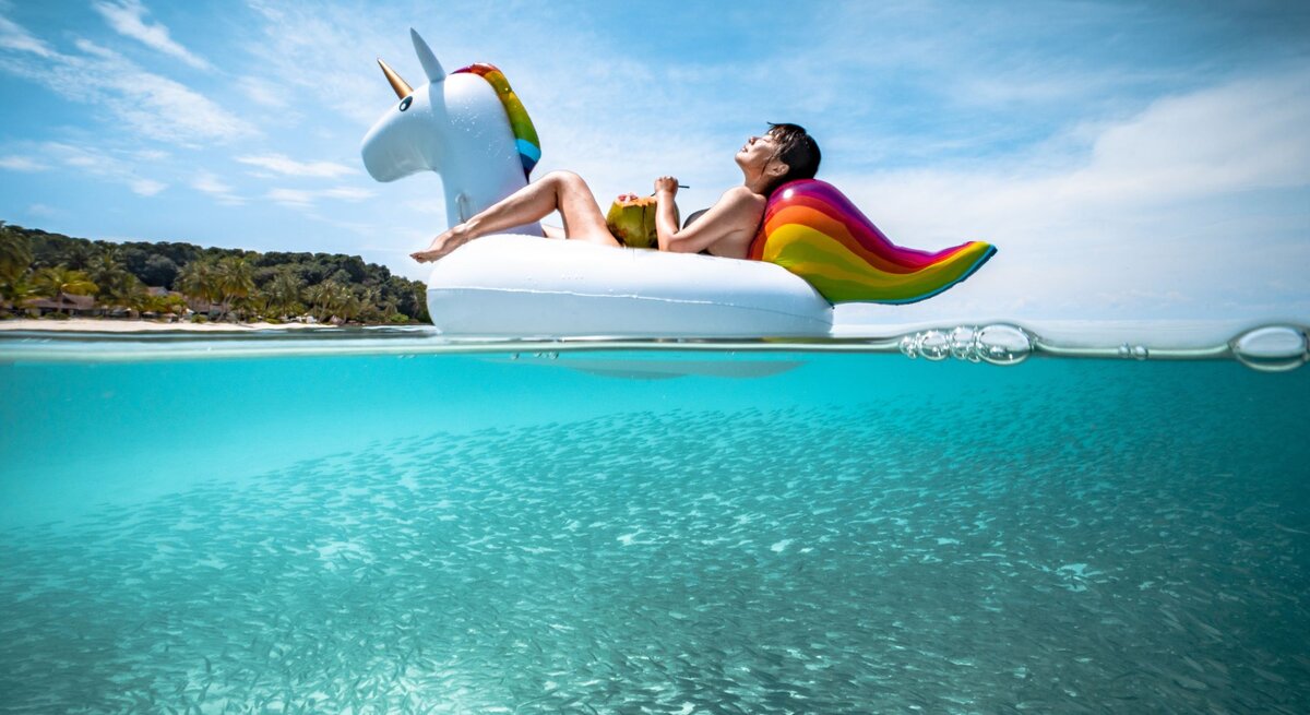 Eine Frau sitzt auf einem aufgeblasenen Einhorn aus Plastik und treibt damit in einem Pool.