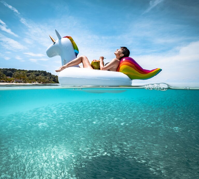 Eine Frau sitzt auf einem aufgeblasenen Einhorn aus Plastik und treibt damit in einem Pool. | © gettyimages/	Khaichuin Sim