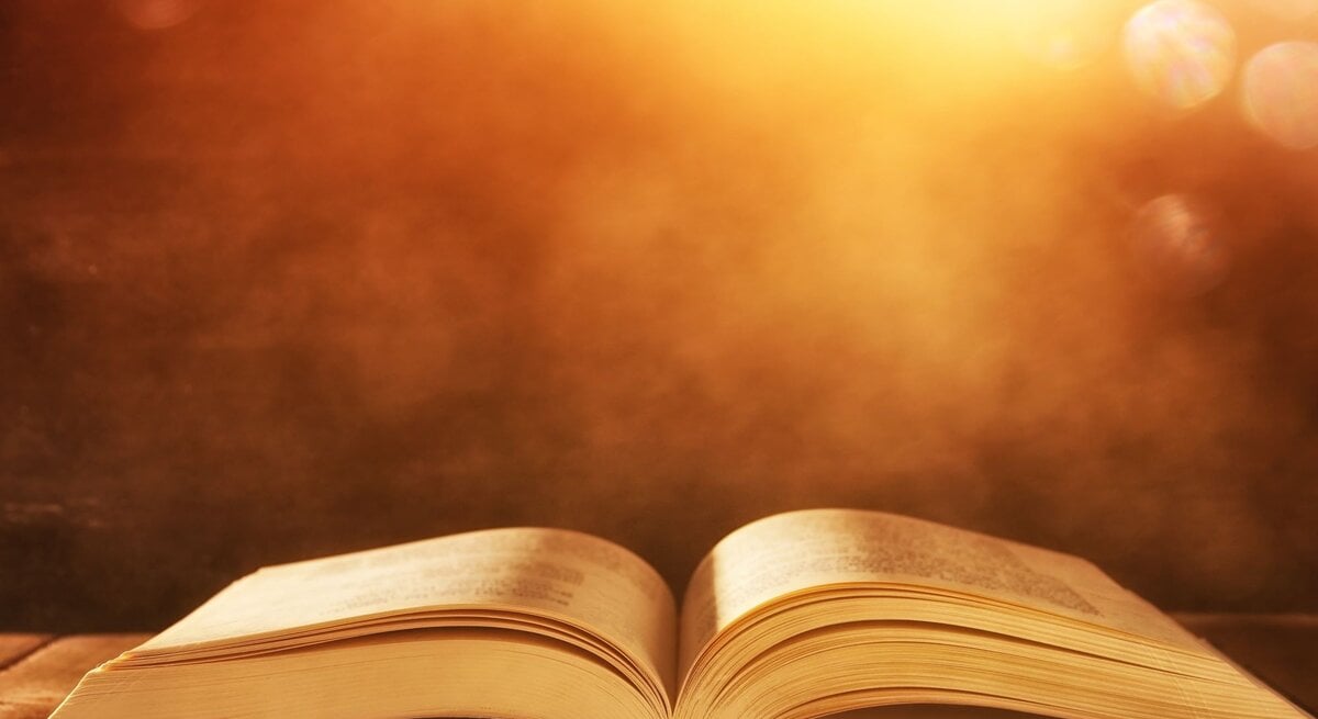 Ein aufgeschlagenes Buch liegt auf einem Holztisch, beleuchtet von warmem, goldenem Sonnenlicht.