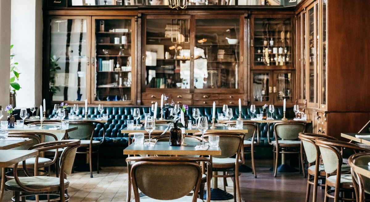 Gemütliches Restaurant mit Holzmöbeln, grüner Ledersitzbank, Kerzen und Weinflaschen, bereit für die Abendgäste.