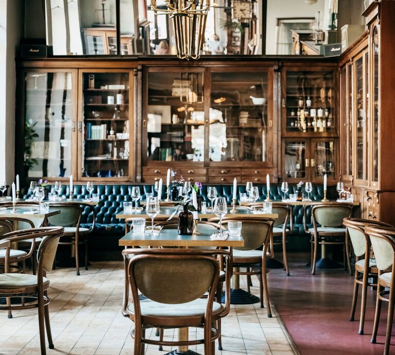 Gemütliches Restaurant mit Holzmöbeln, grüner Ledersitzbank, Kerzen und Weinflaschen, bereit für die Abendgäste. | © Getty Images/Tom Werner