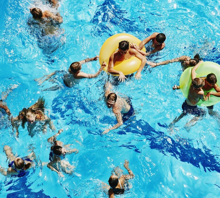 Mehrere Badegäste im Wasser eines Schwimmbeckens, auch Schwimmringe sind mit dabei, alle genießen sichtlich den sonnigen Tag. | © Getty Images/Thomas Barwick