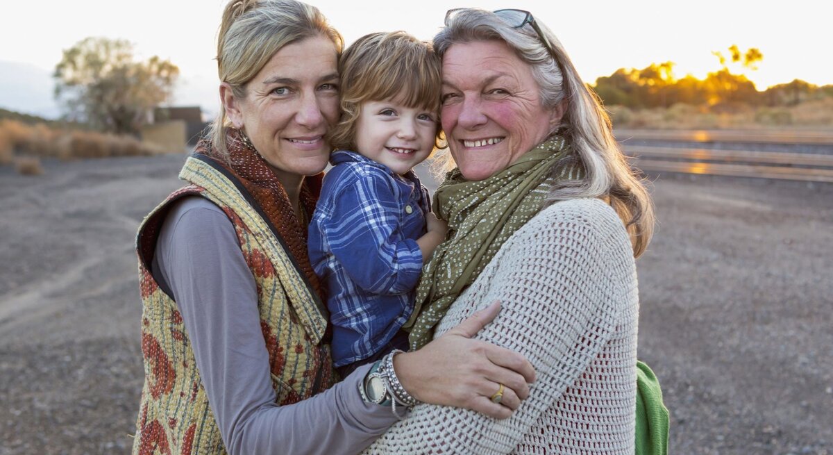 Oma, Mutter und Sohn halten sich im Arm und gucken den Betrachter an.