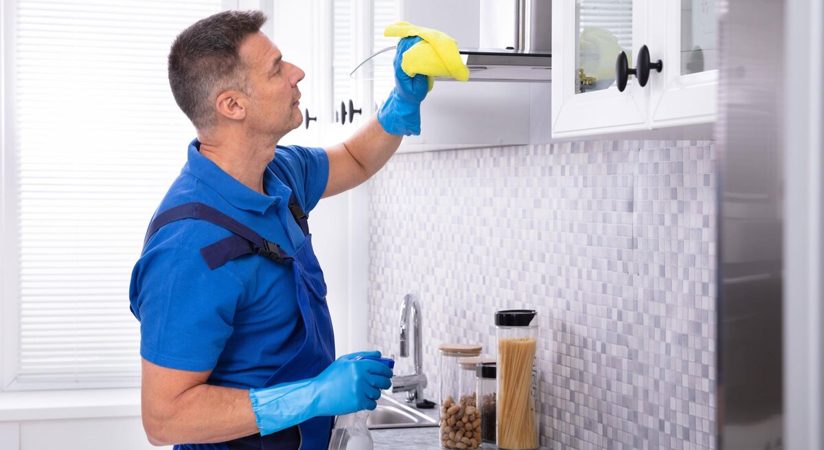 Ein Mann reinigt mit einem Lappen und Handschuhen die Dunstabzugshaube.