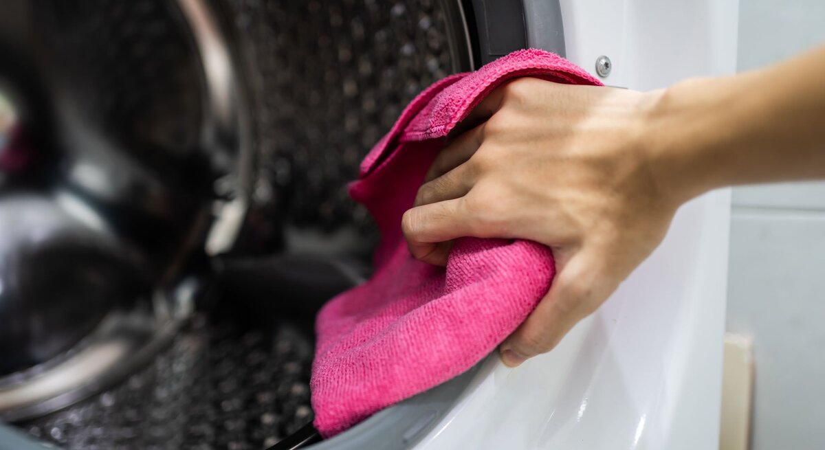 Die Hand einer Frau mit einem Lappen in der Hand, sie putzt die Trommel einer Waschmaschine 