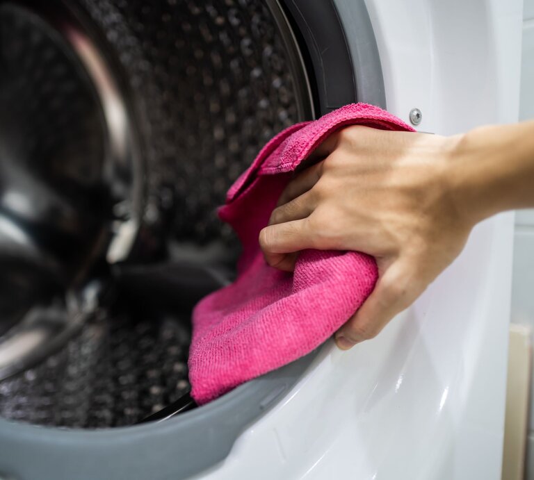Die Hand einer Frau mit einem Lappen in der Hand, sie putzt die Trommel einer Waschmaschine  | © GettyImages/Wachiwit