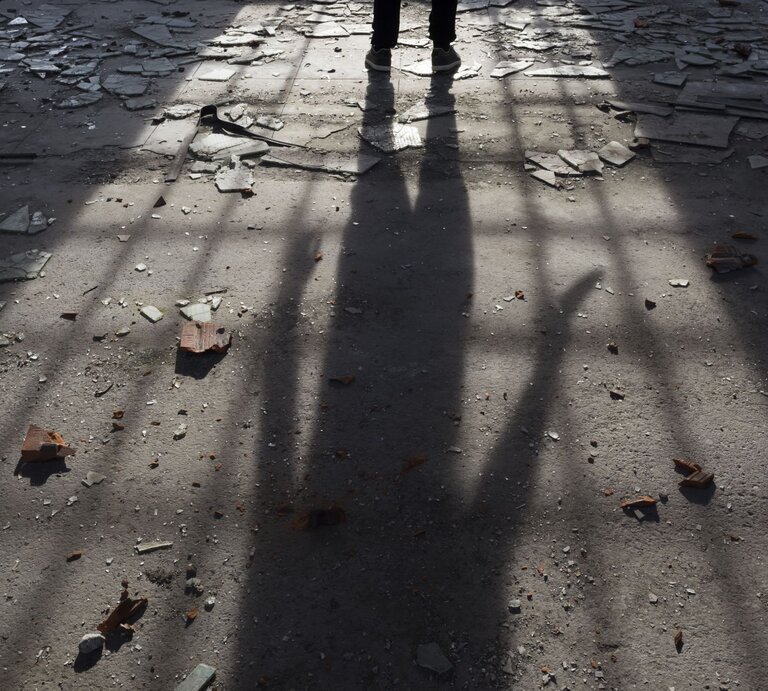  Der Schatten einer Person, die ein Messer hält, fällt bedrohlich auf einen mit Scherben übersäten Boden, was eine düstere und möglicherweise gefährliche Szene suggeriert, während das Tageslicht durch eine unbekannte Struktur ein düsteres Muster auf den Untergrund wirft. | © gettyimages/Marccophoto