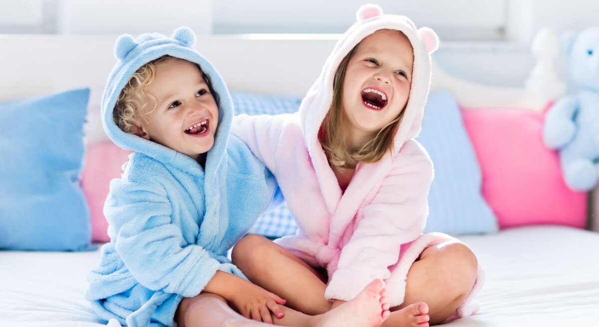 Zwei Kinder tragen Bademäntel in rosa und blau.
