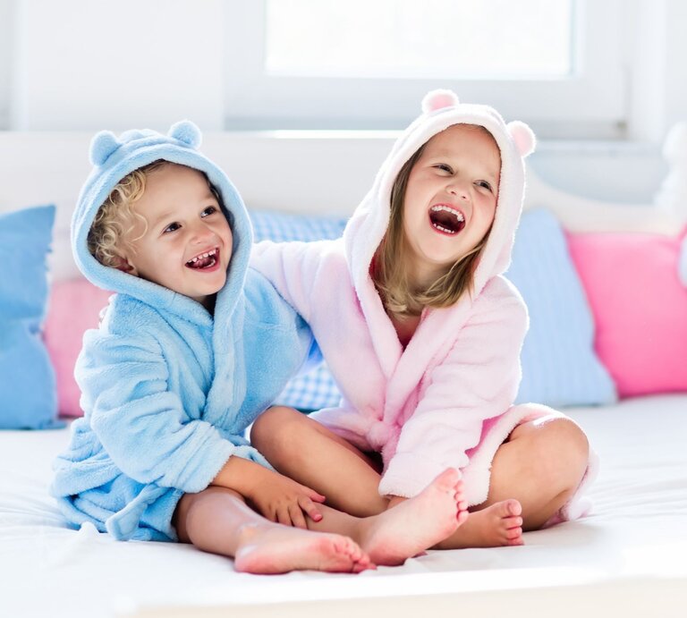 Zwei Kinder tragen Bademäntel in rosa und blau. | © Shutterstock/FamVeld