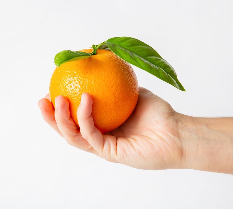 Jemand hält eine Orange in der Hand. | © Shutterstock/Mangostar