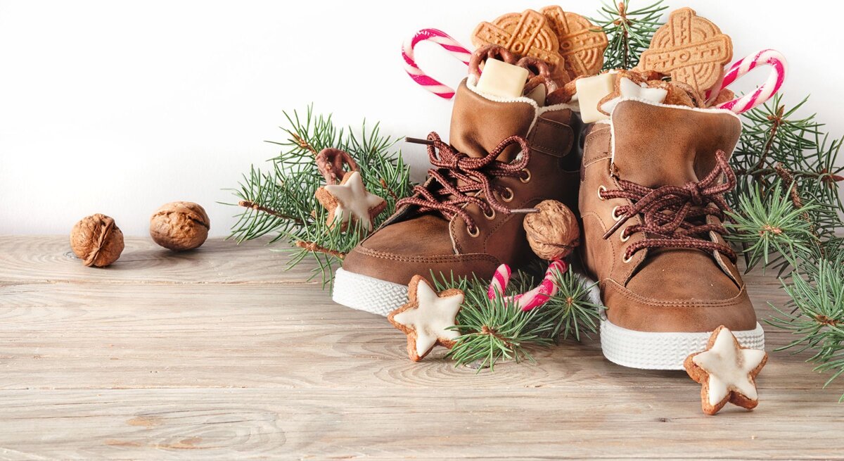 Nikolaus Sprüche: Gefüllte Winterstiefel mit Zuckerstangen, Nüssen und Zimtsternen stehen festlich zwischen Tannengrün auf Holz.