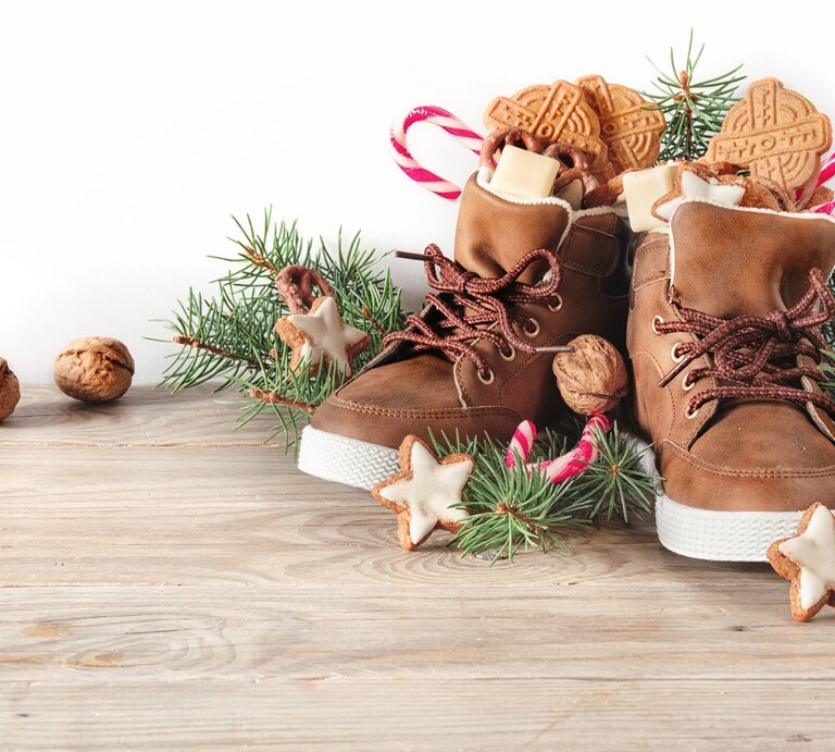 Nikolaus Sprüche: Gefüllte Winterstiefel mit Zuckerstangen, Nüssen und Zimtsternen stehen festlich zwischen Tannengrün auf Holz. | © Shutterstock/ tilialucida