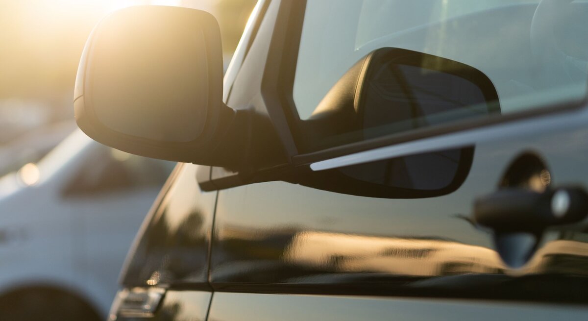 Ein parkendes schwarzes Auto, dessen Seitenspiegel von der untergehenden Sonne angestrahlt wird, daneben ein weißes Fahrzeug.