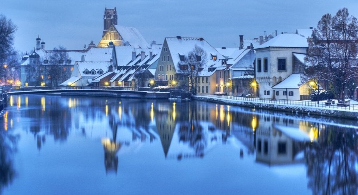 Eine verschneite Altstadt am Abend. Die Lichter spiegeln sich im Fluss.