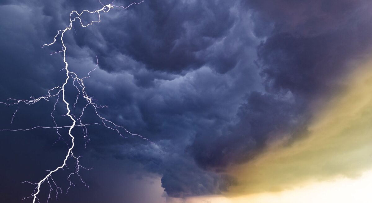 Ein Blitz erhellt dramatisch den dunklen Himmel über einem abgeernteten Feld mit Windrädern im Hintergrund.