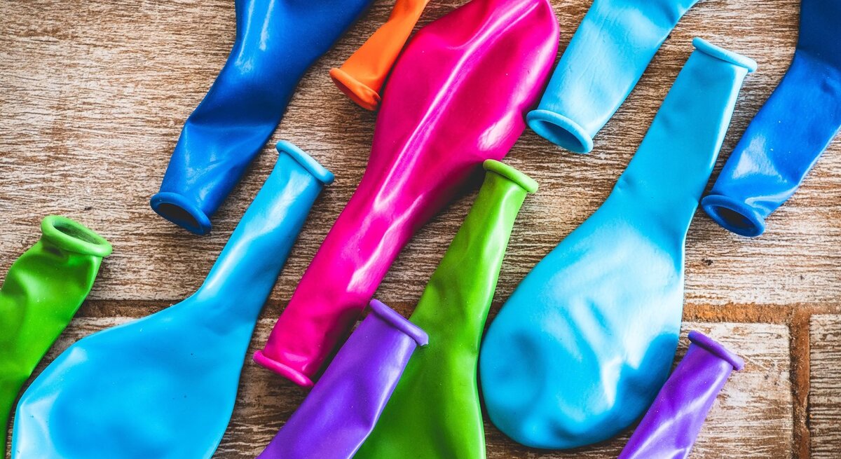 Bunte, unaufgeblasene Luftballons in verschiedenen Farben liegen verstreut auf hellem Holz.