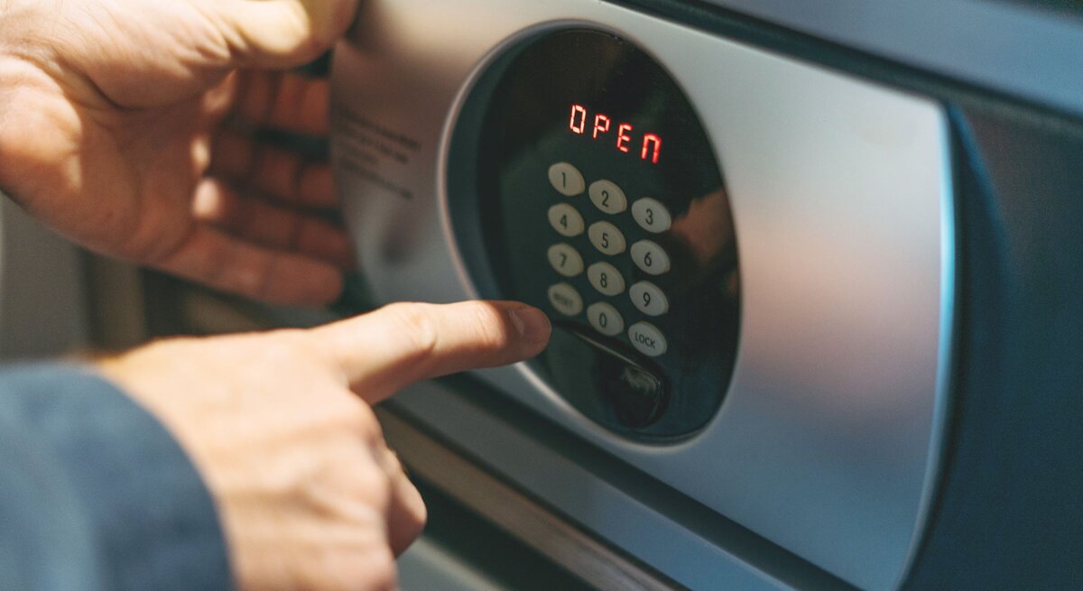 Nahaufnahme von Händen, die einen geöffneten Safe durch Eingabe des Zahlencodes entriegeln.