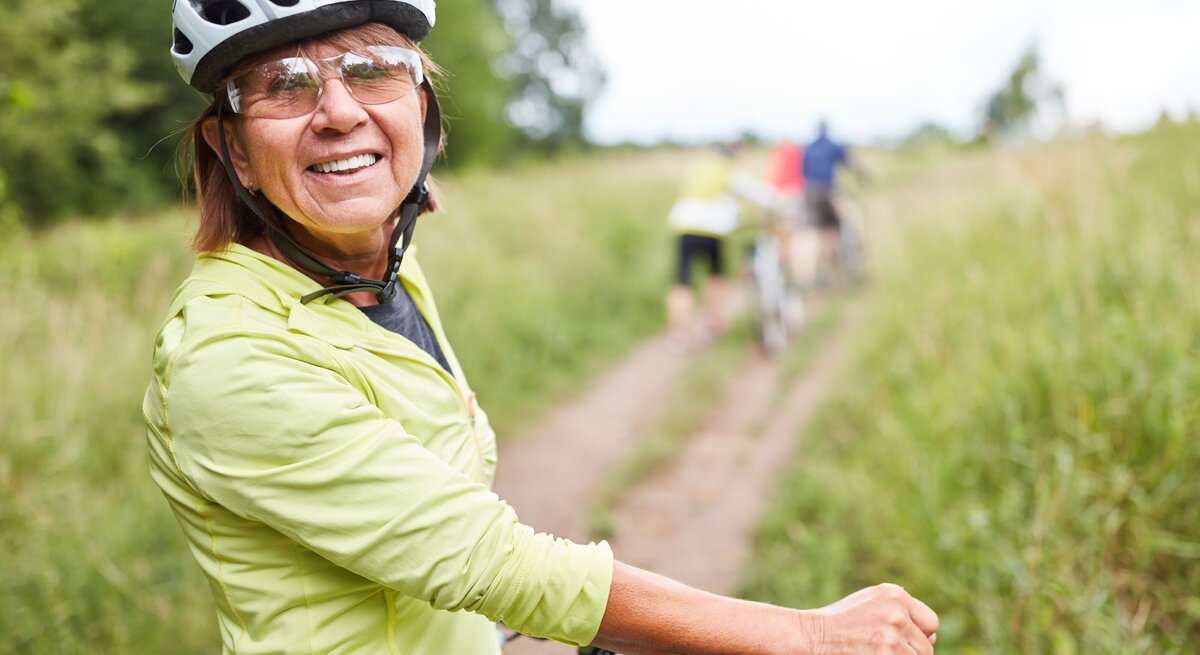 Ältere Frau auf dem Fahrrad trägt einen Fahrradhelm in der Natur.